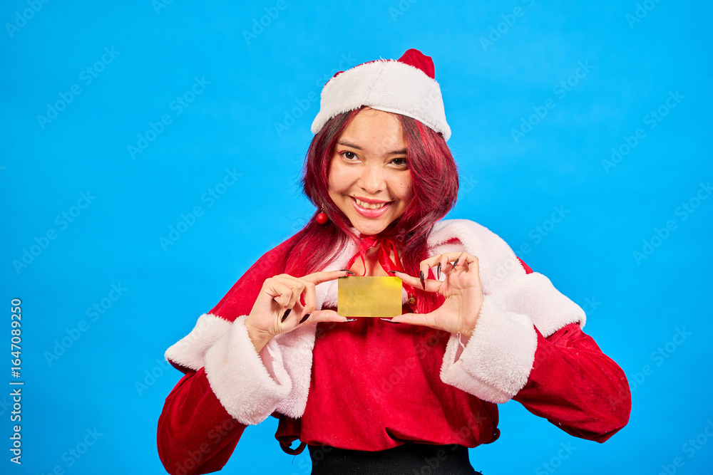 Obraz premium Smiling woman wearing santa costume showing gold credit card on blue background