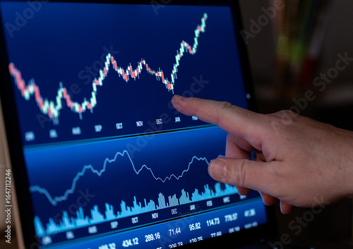 Finger pointing at a stock market chart on a computer screen. Trading board, stock exchange, research, business, financial figures, analyzing, investment.