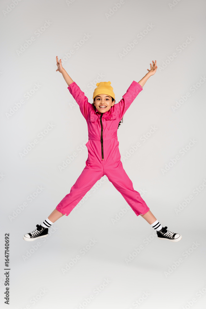 Fototapeta premium Trendy preteen girl joyfully jumps in pink overalls