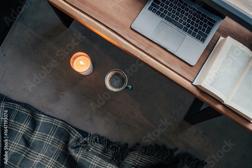 Cozy Work Corner: Overhead view of a warm-toned desk with a candle, book, coffee cup, and laptop