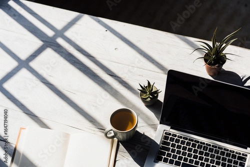 Home Office Surrounded by Plants: Flat lay of a wooden desk with laptop, cup of tea, and small potted plants, bright natural daylight, airy composition with negative space