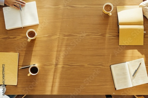 Office Meeting Table: Overhead shot of a few notebooks, coffee cups, and pens spread out on a large wooden table