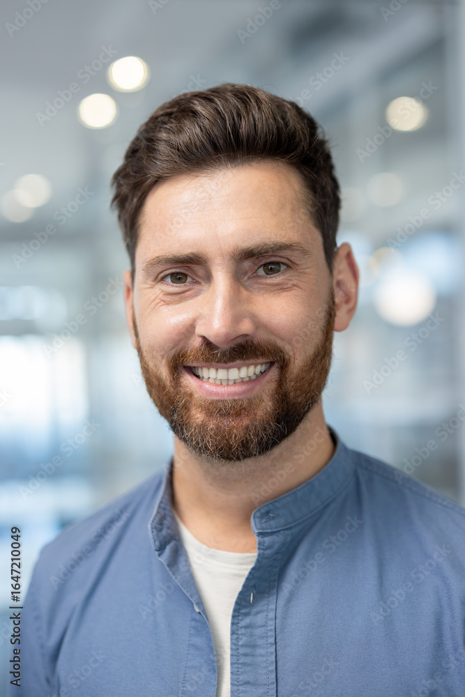 A cheerful man smiles warmly in a bright, modern office setting. Natural light enhances the welcoming and professional atmosphere, conveying positivity and approachability. A cheerful man smiles warmly in a bright, modern office setting. Natural light enhances the welcoming and professional atmosphere, conveying positivity and approachability.
