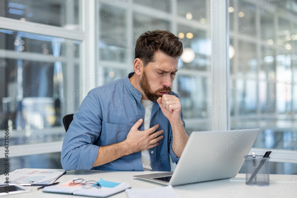 Fototapeta premium A male professional experiencing discomfort in his chest as he coughs while at work in an office. This image conveys health-related struggles in a business environment.