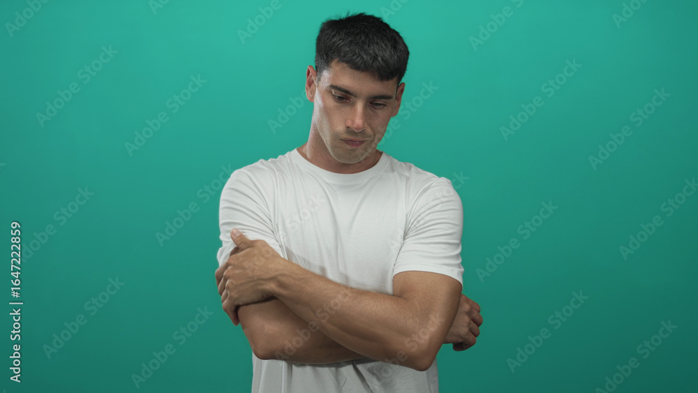 Fototapeta premium Man holds arm in front of green background in studio, gripping his visible forearm with downcast gaze; contemplation.