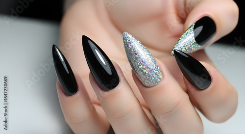 Close up of a woman's hand with black and glittery silver stiletto nails