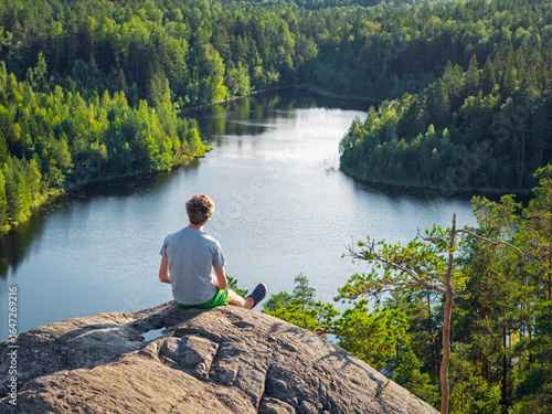 A man sits on a rock and contemplates a forest lake