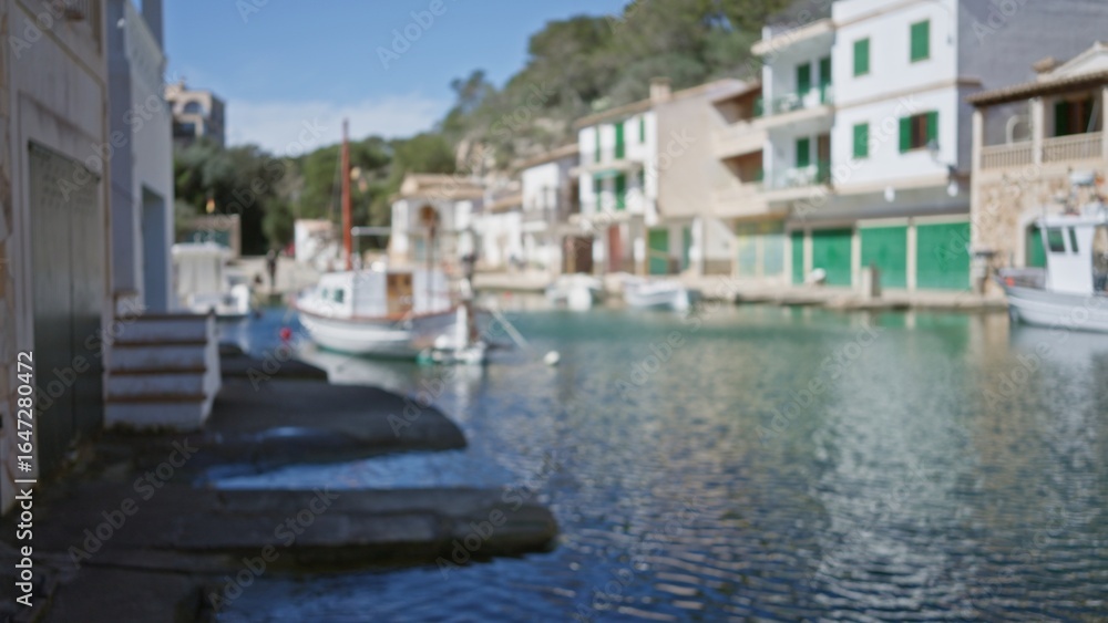 Obraz premium Blurred view of scenic cala figuera port in mallorca showcasing boats along calm waters and charming waterfront buildings under a bright sky.