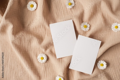 Two white cards on soft beige cloth with chamomile flowers flat lay