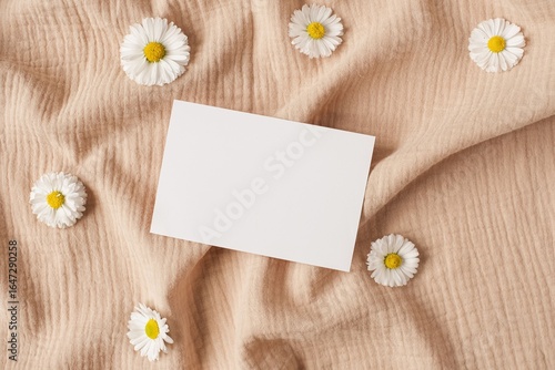 Single white card on beige fabric surrounded by chamomile flowers
