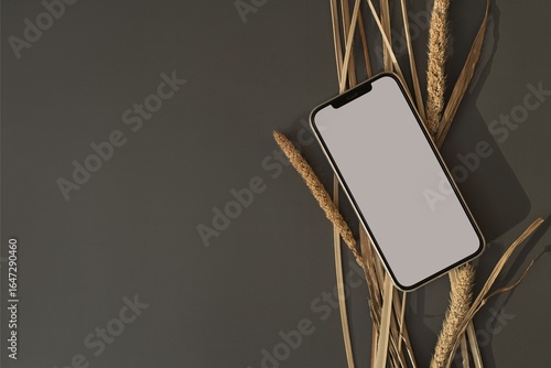White tablet with blank screen on peach surface with dried grass decoration