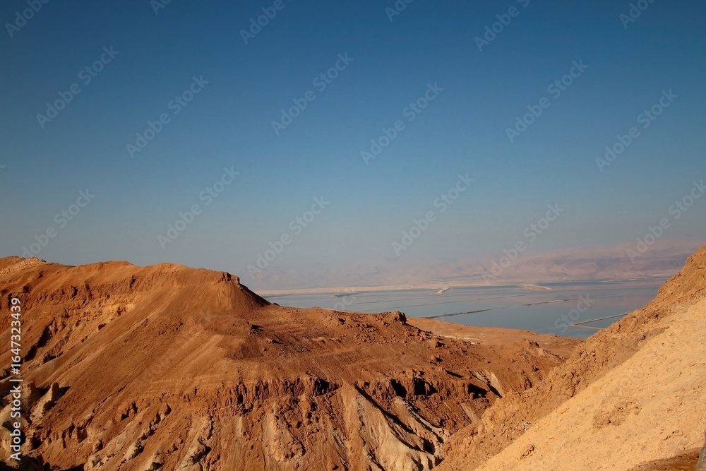 Fototapeta premium Warm sunset glow over rugged cliffs near the Dead Sea, highlighting the contrast between golden light and arid terrain.