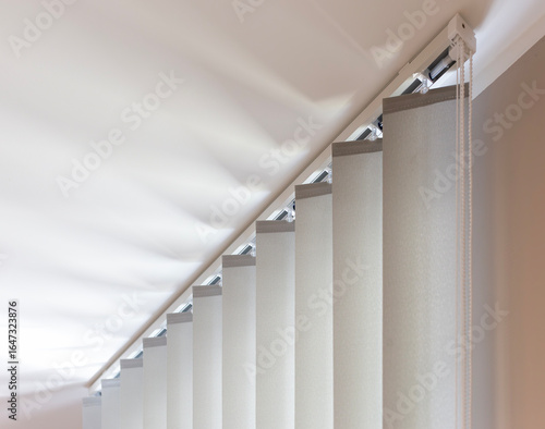 The top section of beige vertical blinds is shown in detail, highlighting the rail and control chain mechanism, providing both sun protection and privacy for modern home or office interiors.