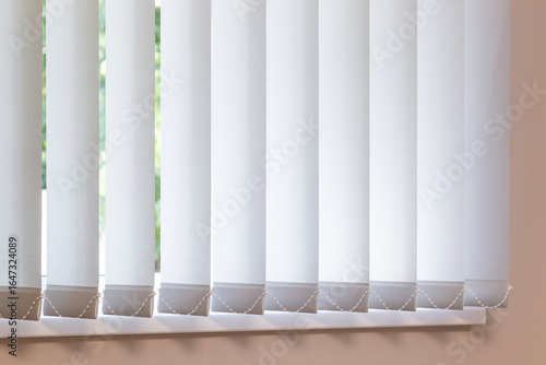 Vertical blinds covering a bright window, ideal for offices, living rooms, or bedrooms. These vertical fabric blinds offer light control, privacy, and modern style for both home and workspace interior