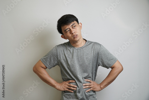 A young Asian man holds his stomach with both hands, with a grimacing expression of pain and discomfort.