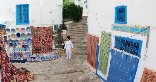 Sidi bou Said, Tunisia - Jan 11, 2025: Stylish tourist woman Exploring Sidi Bou Said Charming Streets and Artisan Market, aerial view