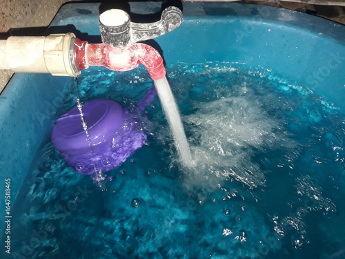 Water flows from the faucet into the bathtub. The faucet appears slightly leaky and dirty up close. Bathroom background.