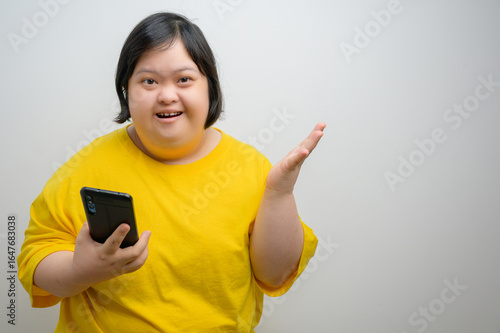 Young woman with Down syndrome wearing yellow shirt holding smartphone and smiling, indoor portrait, diversity, inclusion, disability awareness, happiness and communication concept.