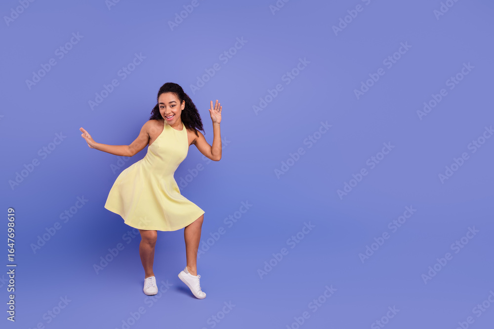 Cheerful young woman dancing joyfully in a vibrant yellow dress against a solid pastel purple background in a studio Cheerful young woman dancing joyfully in a vibrant yellow dress against a solid pastel purple background in a studio
