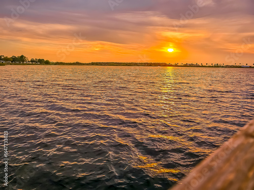 A tranquil sunset over calm waters, where golden light meets rippling reflections beneath a serene, colorful dusk sky and silhouetted horizon.