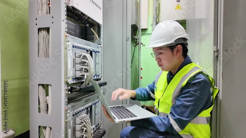 Network technician inspection on server rack cables using laptop in data center wearing safety helmet and reflective vest ensuring data center safety and efficient network maintenance