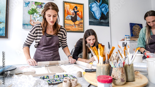 In an art studio  three beautiful middle-aged women friends are happily drawing patterns and painting the vases they made from clay at a table filled with art supplies