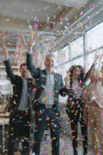 Blurred background of people in business suits celebrating in an office, throwing confetti and holding party streamers. Concept of corporate celebration, team success, and joyful workplace moments.