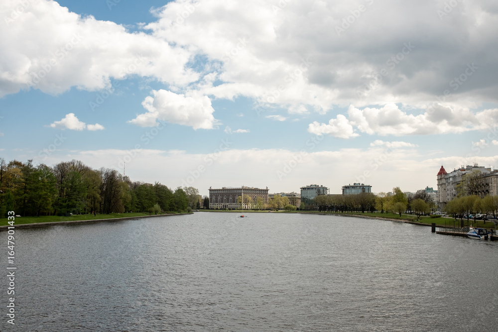 Fototapeta premium Relaxing View of a River With Buildings and Trees on the Banks During a Cloudy Day in a City Park