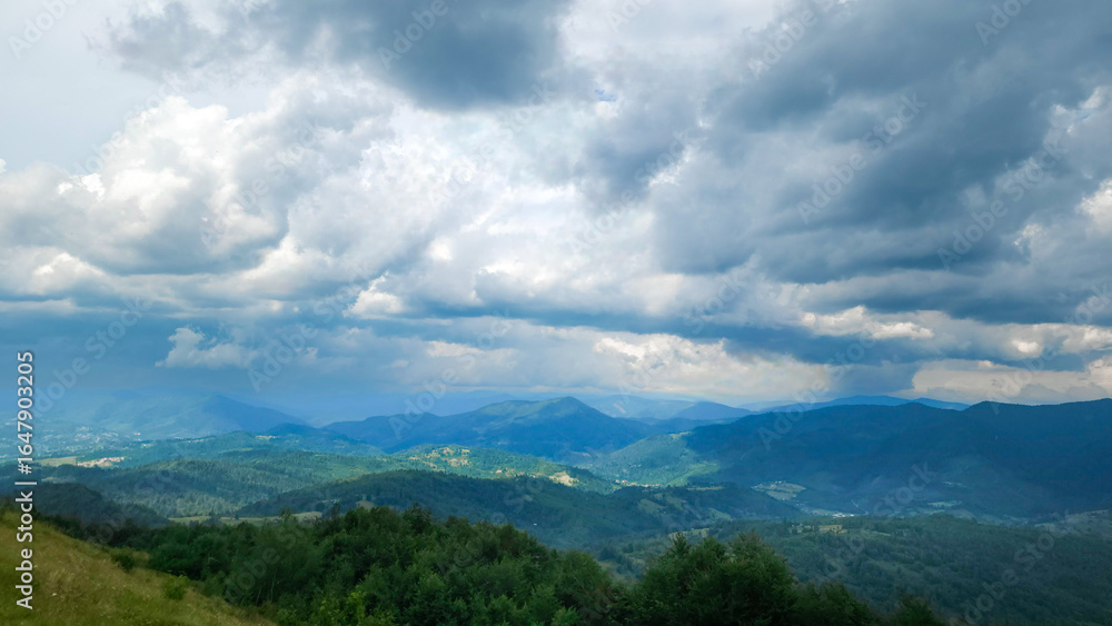 Obraz premium A stunning view of a lush mountain range under a bright blue sky with rolling clouds, perfect for travel, nature, and outdoor adventure promotions