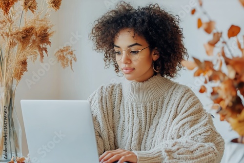 Young Woman Working on Laptop in Cozy Autumn Setting With Plant Decor and War...