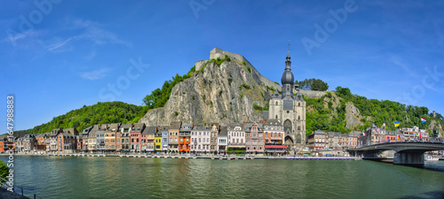  A panoramic view of the Belgian town of Dinant on the Meuse River, featuring the Collegial Church of Our Lady and the historic Citadel perched on a cliff above the colorful buildings along the waterf