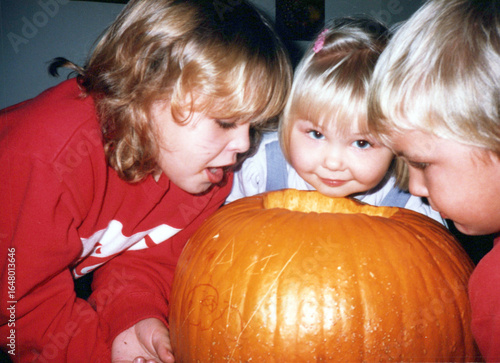 Circa 1991: Siblings carve Halloween pumpkins at the kitchen table in the early 90s. Vintage scan, may have imperfections