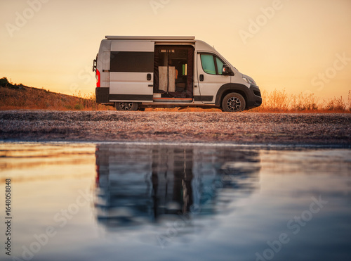 view to white camper van on the alone beach in evening time with reflections in calm water and nobody