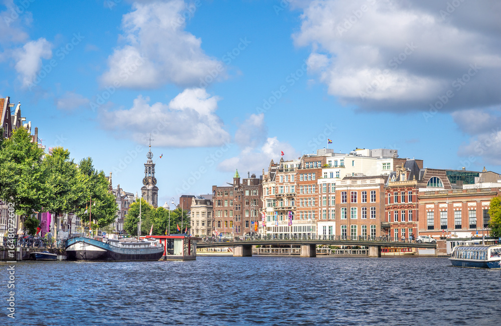 Naklejka premium Navigating the inner Amstel river (Binnenamstel) in the city center of Amsterdam with the historic Muntttoren uin the background, Holland, the Netherlands