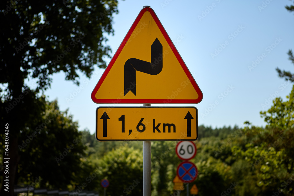 Road sign warning of winding road ahead for 1.6 km in rural area Road sign warning of winding road ahead for 1.6 km in rural area
