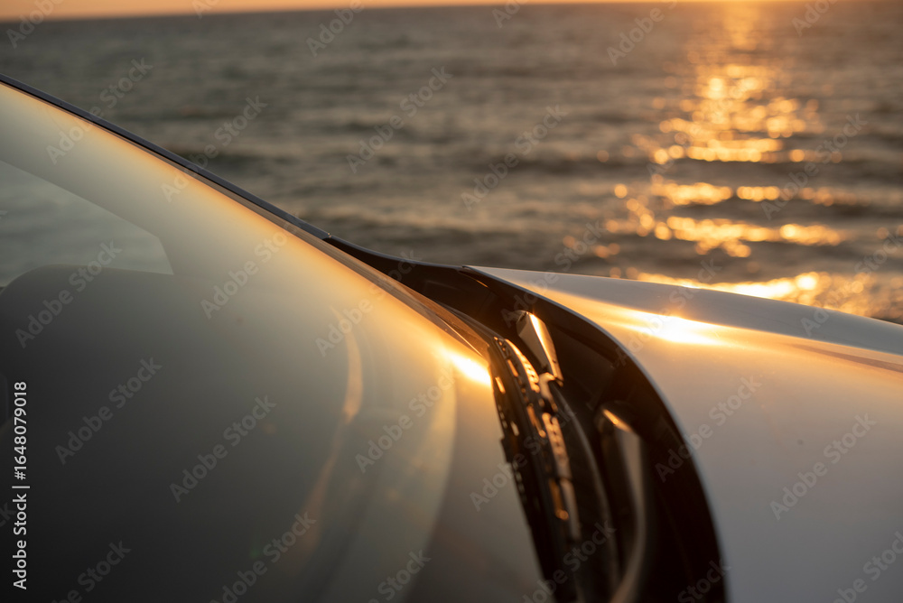 Obraz premium A close-up of a car's windshield with sunlight reflecting off the water in the background. The scene conveys a sense of freedom and adventure by the sea.