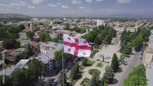 Aerial View of Gori, Georgia with Waving National Flag and Historic Fortress. A stunning aerial view featuring the Georgian national flag waving in the foreground, the historic Gori Fortress on a hill