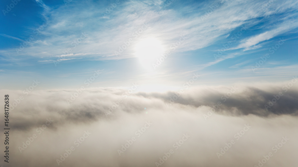 Obraz premium Bright sunlight pierces through fluffy clouds, illuminating a serene blue sky above a sea of misty clouds below.