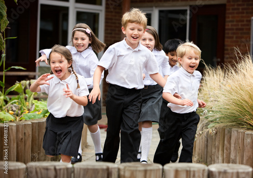 Cheerful primary students running outdoors. A group of happy children in school uniforms laughing and playing in a school playground during break time.