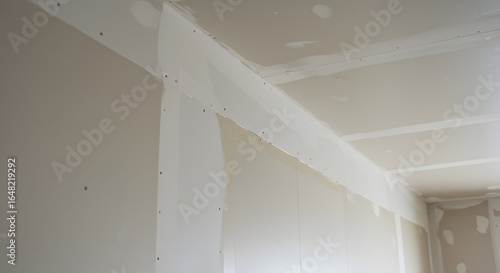 Unfinished room interior with newly installed drywall. Gypsum board walls and ceiling showing taped seams and screws during construction or renovat...