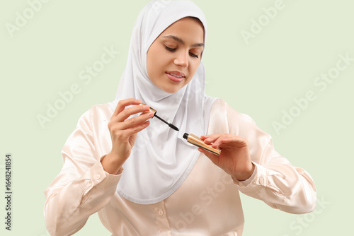 Pretty young woman in hijab with mascara on light green background