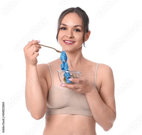 Young woman in underwear with bowl and fork eating measuring tape on white ba...