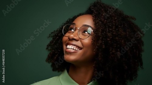 Smiling woman with glasses looking upwards against green backdrop portrait