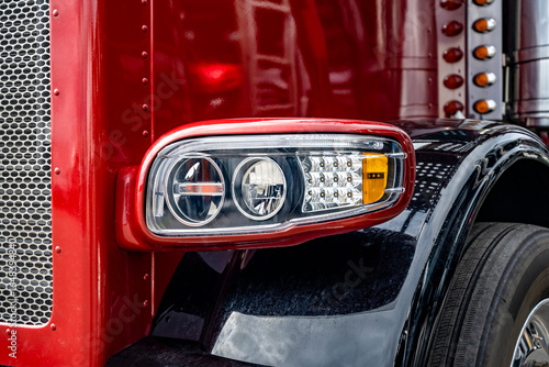 Front part of the red big rig classic semi truck with chrome details and black fenders with shiny reflective surface
