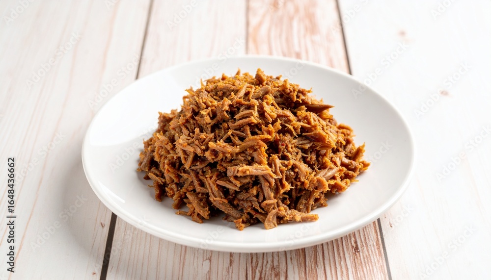 A savory portion of traditional slow-cooked shredded beef, a classic ropa vieja dish, served neatly on a white plate against a light wooden background. A savory portion of traditional slow-cooked shredded beef, a classic ropa vieja dish, served neatly on a white plate against a light wooden background.