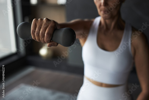 Canvas Print Middle aged Caucasian woman exercising indoors, holding dumbbell with outstretch