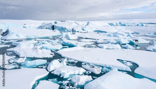 Aerial view reveals stunning icebergs and turquoise meltwater pools scattered across a vast, icy landscape under a partly cloudy sky in the antarctic region.