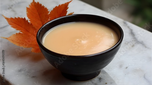 Creamy, smooth soup in a dark bowl with autumnal leaves.