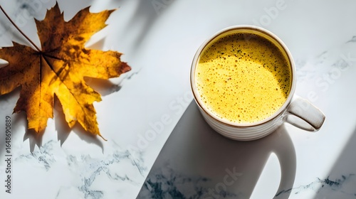 Golden drink and autumn leaf on a white marble surface.