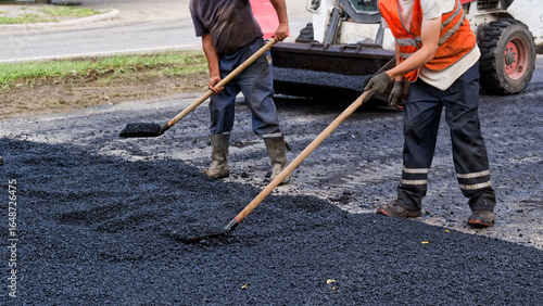 Fotografija Unrecognizable road crew spreads and levels fresh asphalt by hand with rake and shovel during street repair; curbside maintenance and landscaping upgrade in progress